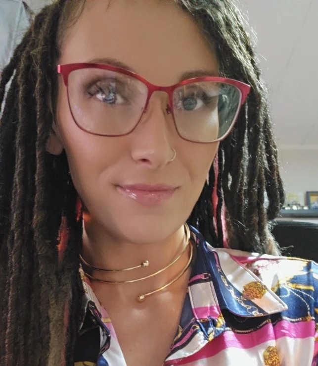 Headshot of woman with brown dreadlocks and red framed glasses.