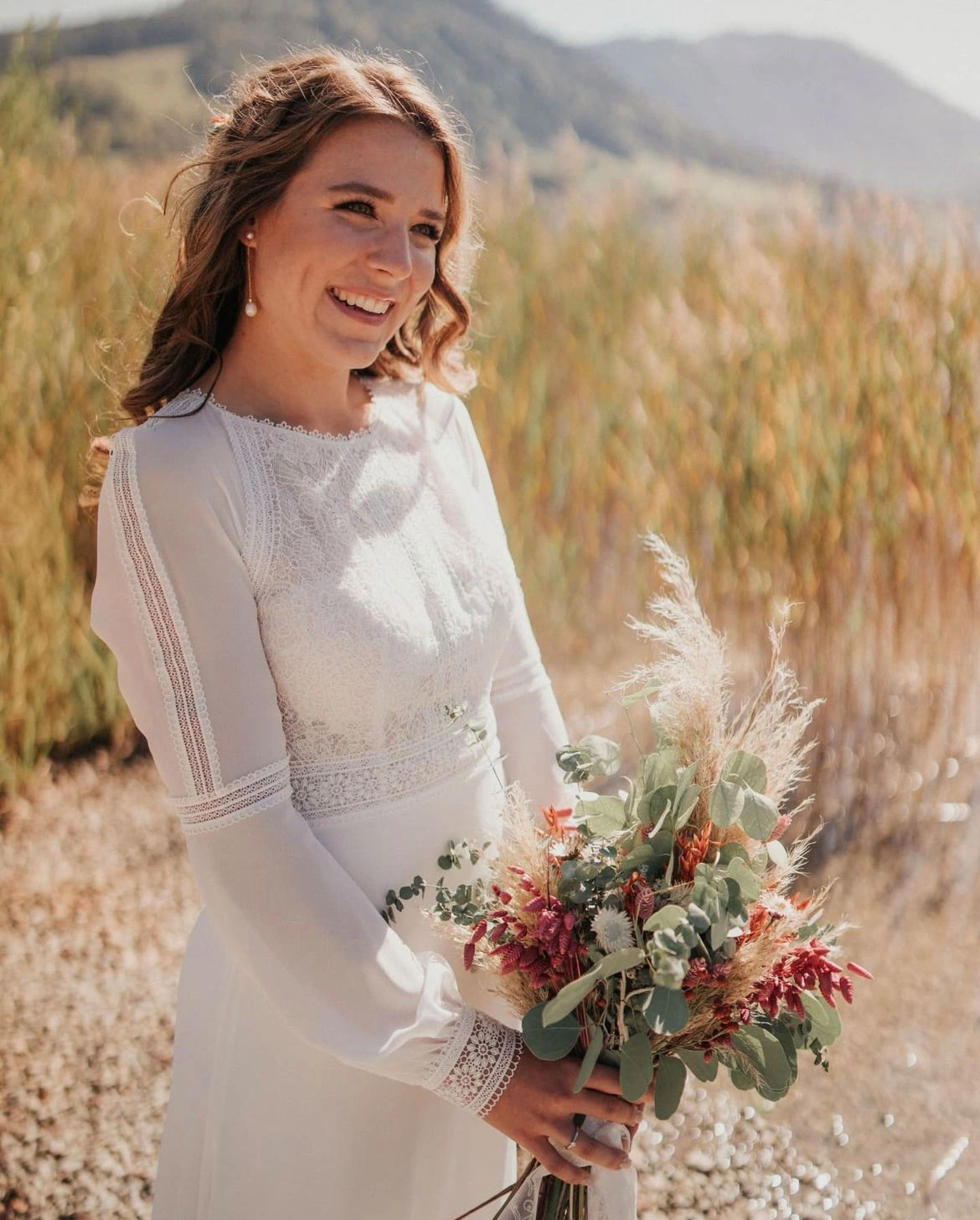 Braut mit weißem Hochzeitskleid und Blumenstrauß steht in einem Feld. Make-up von Denise Drahtmueller