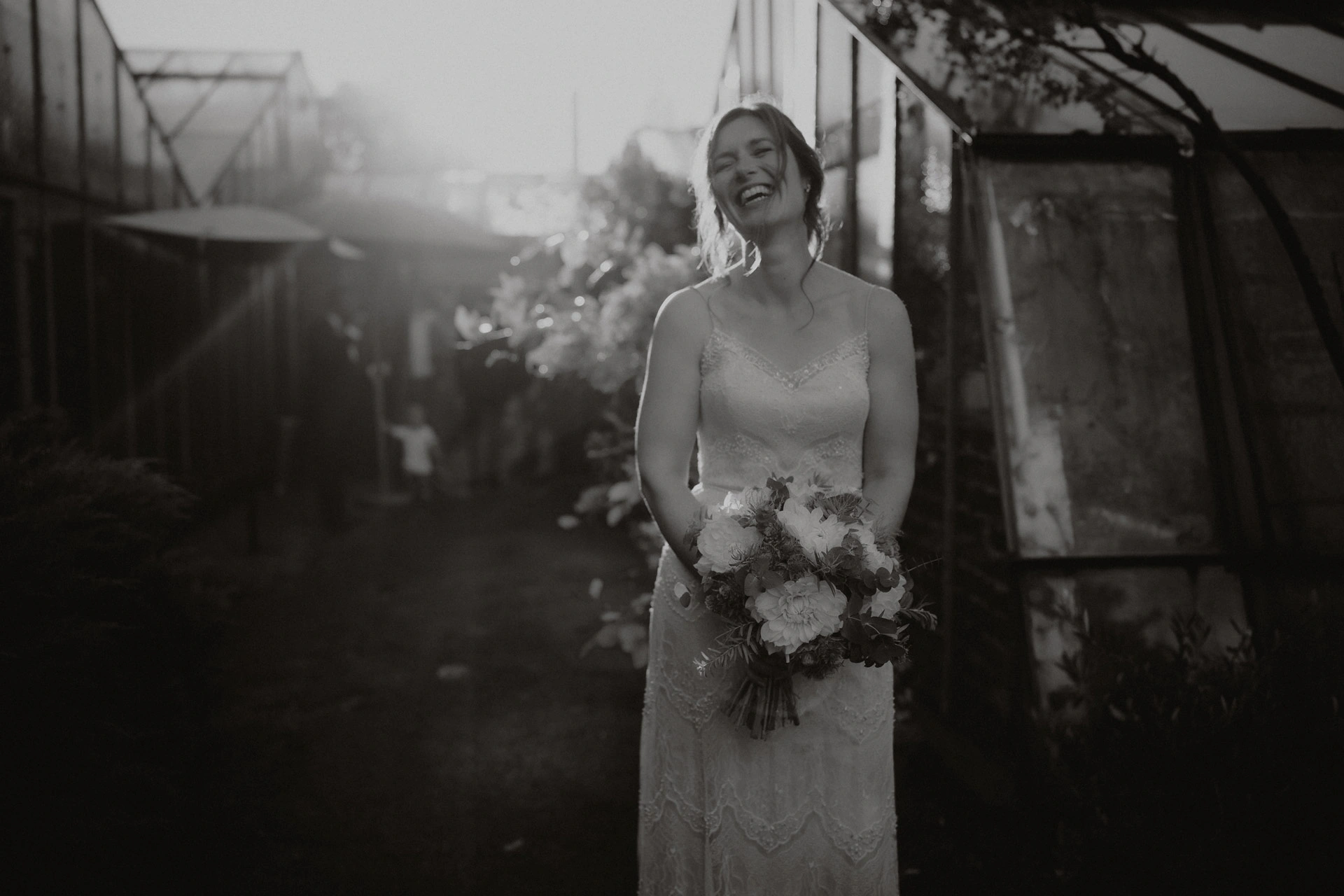 Braut steht mit Kleid und Brautstrauß in einem Garten. Haare und Make-up von Denise Drahtmueller