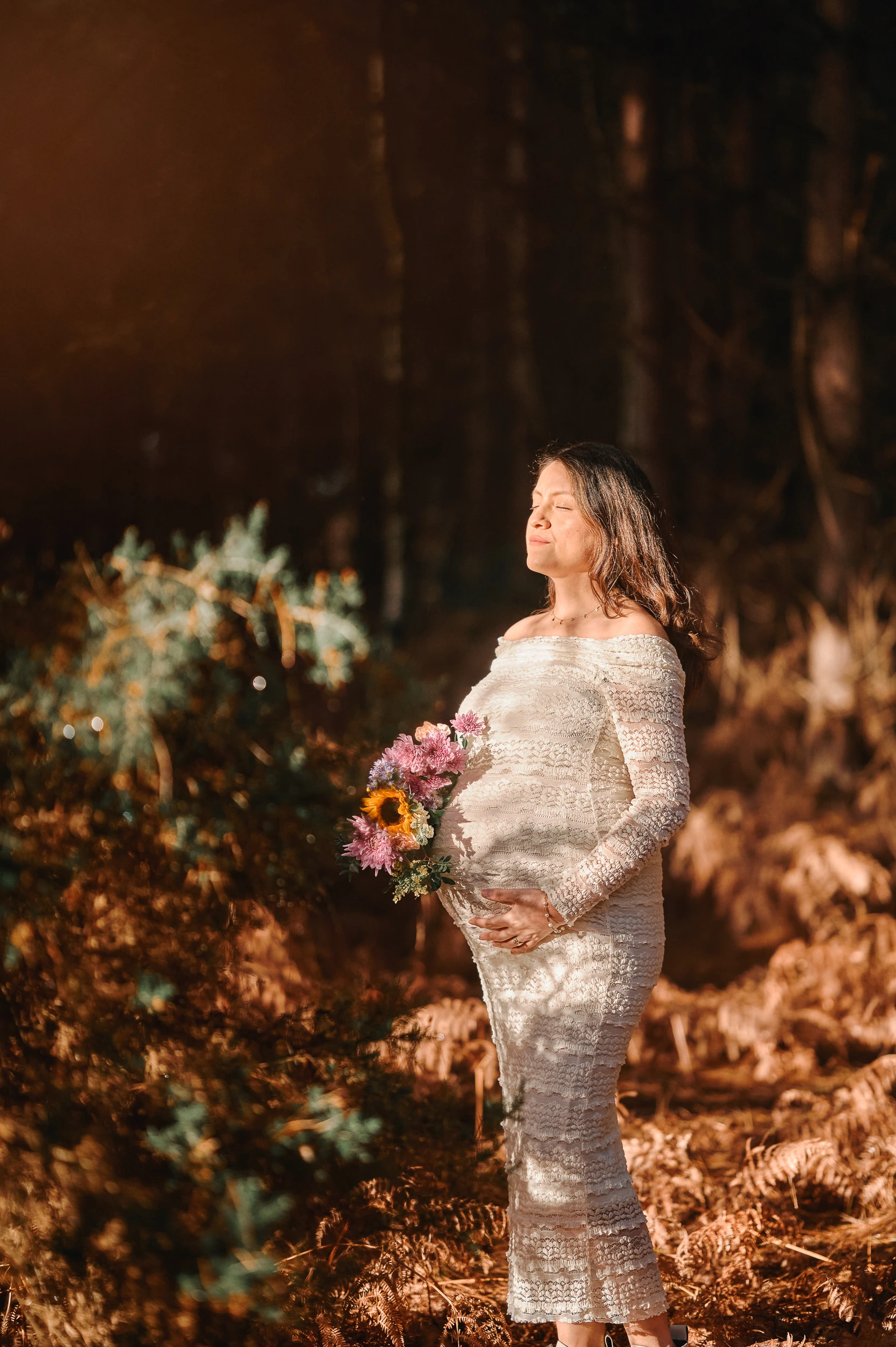 woman holding flowers over pregnancy bump in the forest