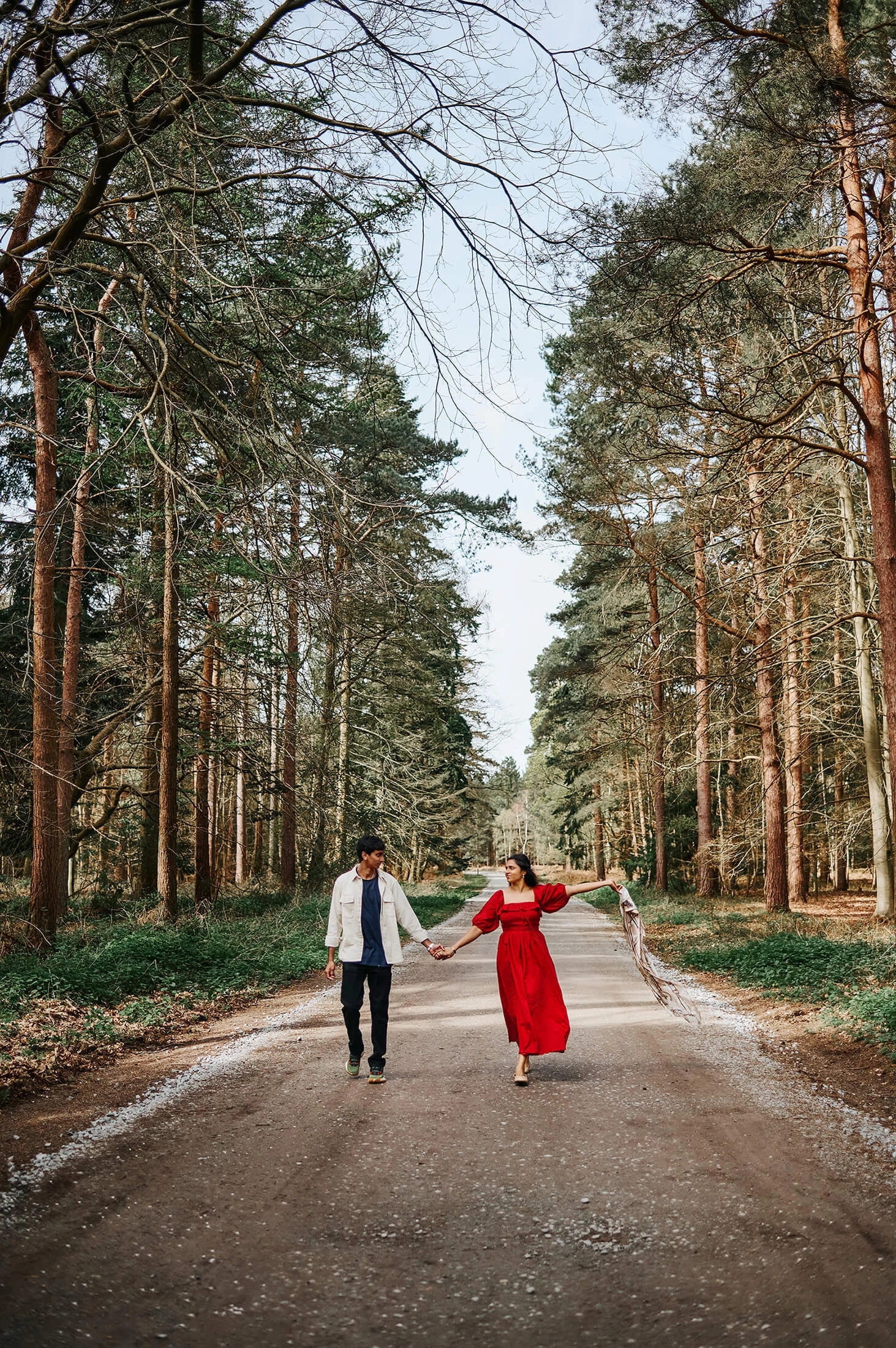 Couple holding hands while walking together, with a scarf lifted in the air during a natural outdoor photography session