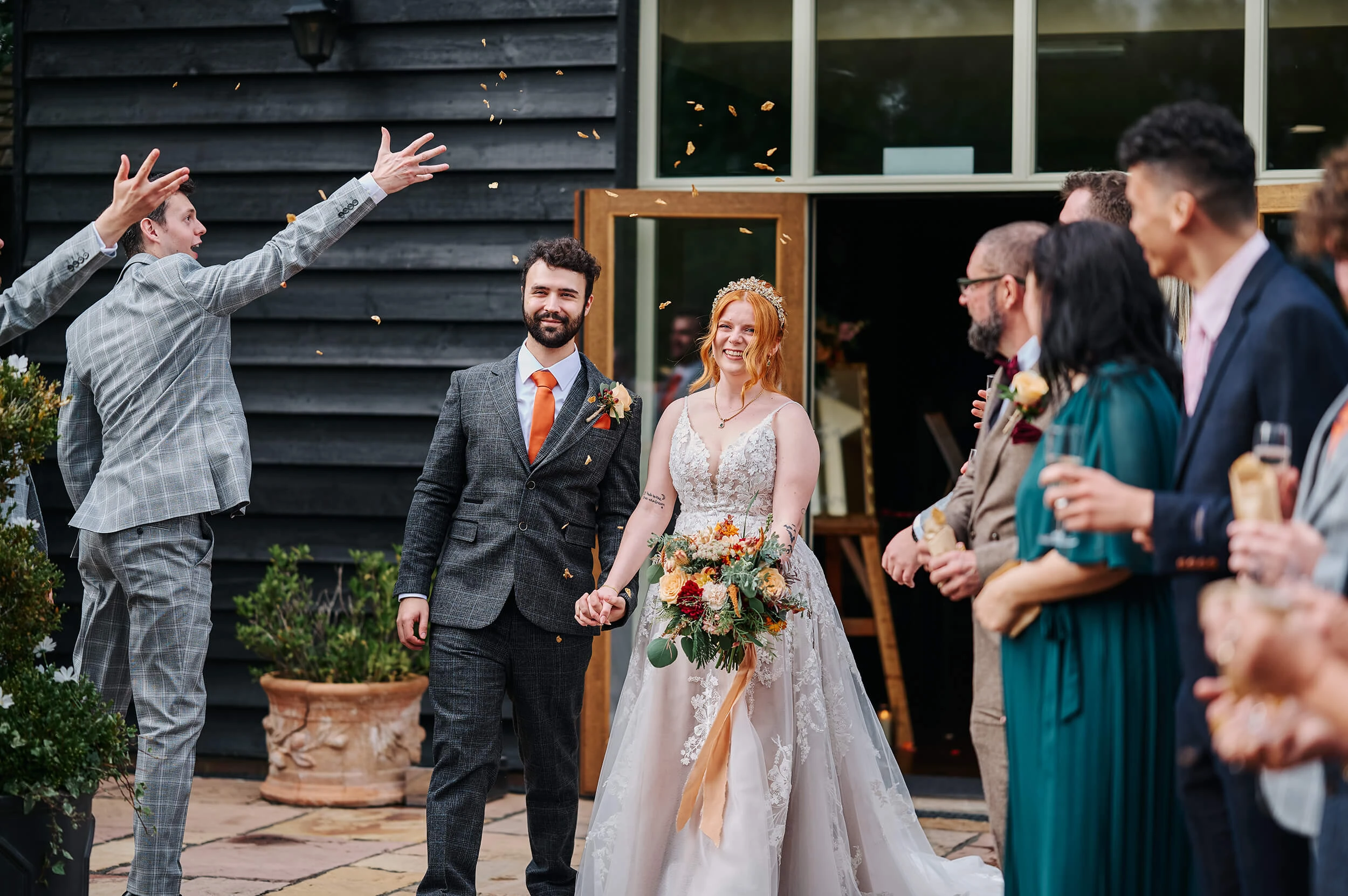 Bride and groom walking through confetti outside The White Hart wedding venue in Essex