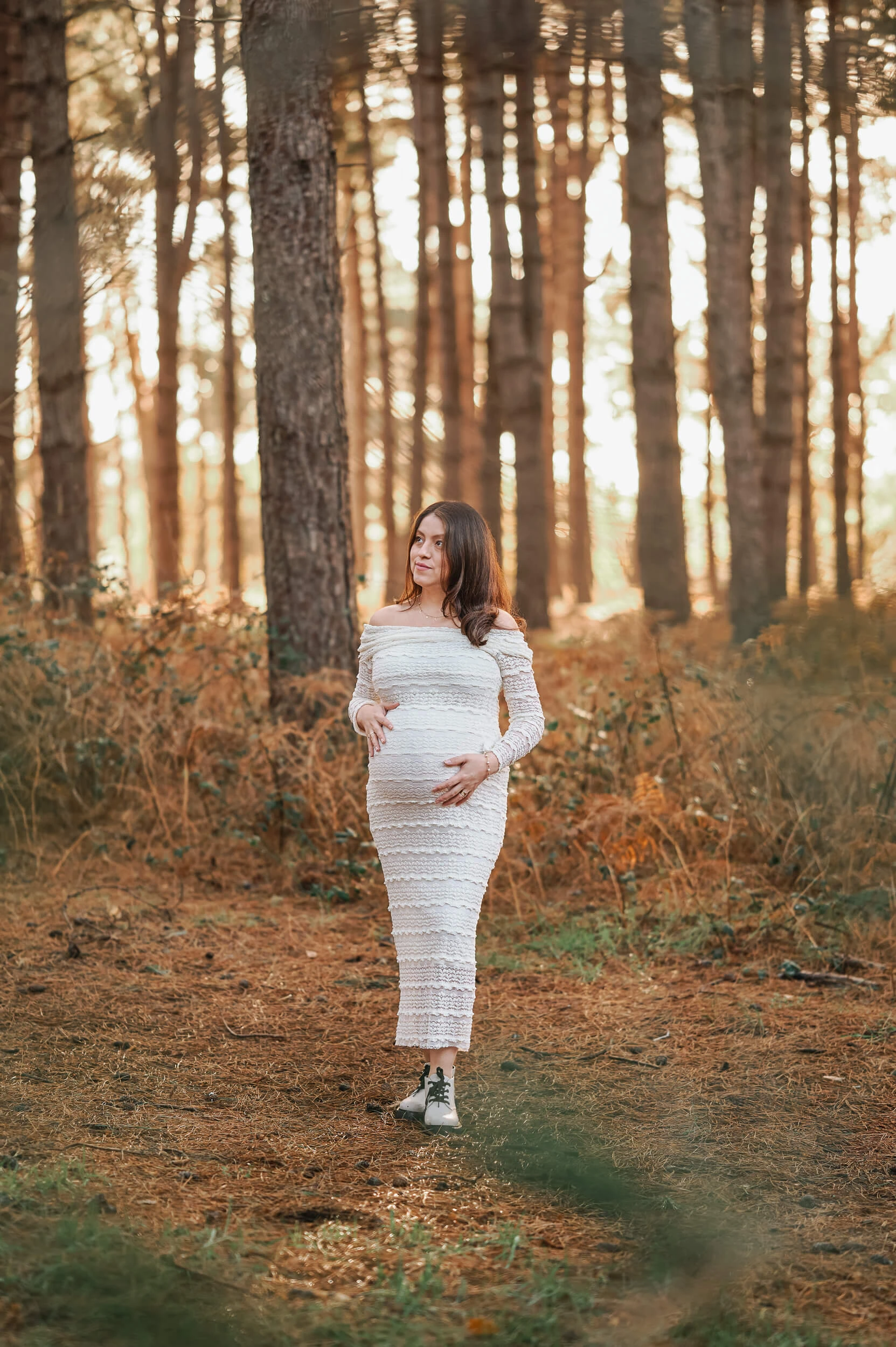 maternity photo shoot under tall trees in winter smiling
