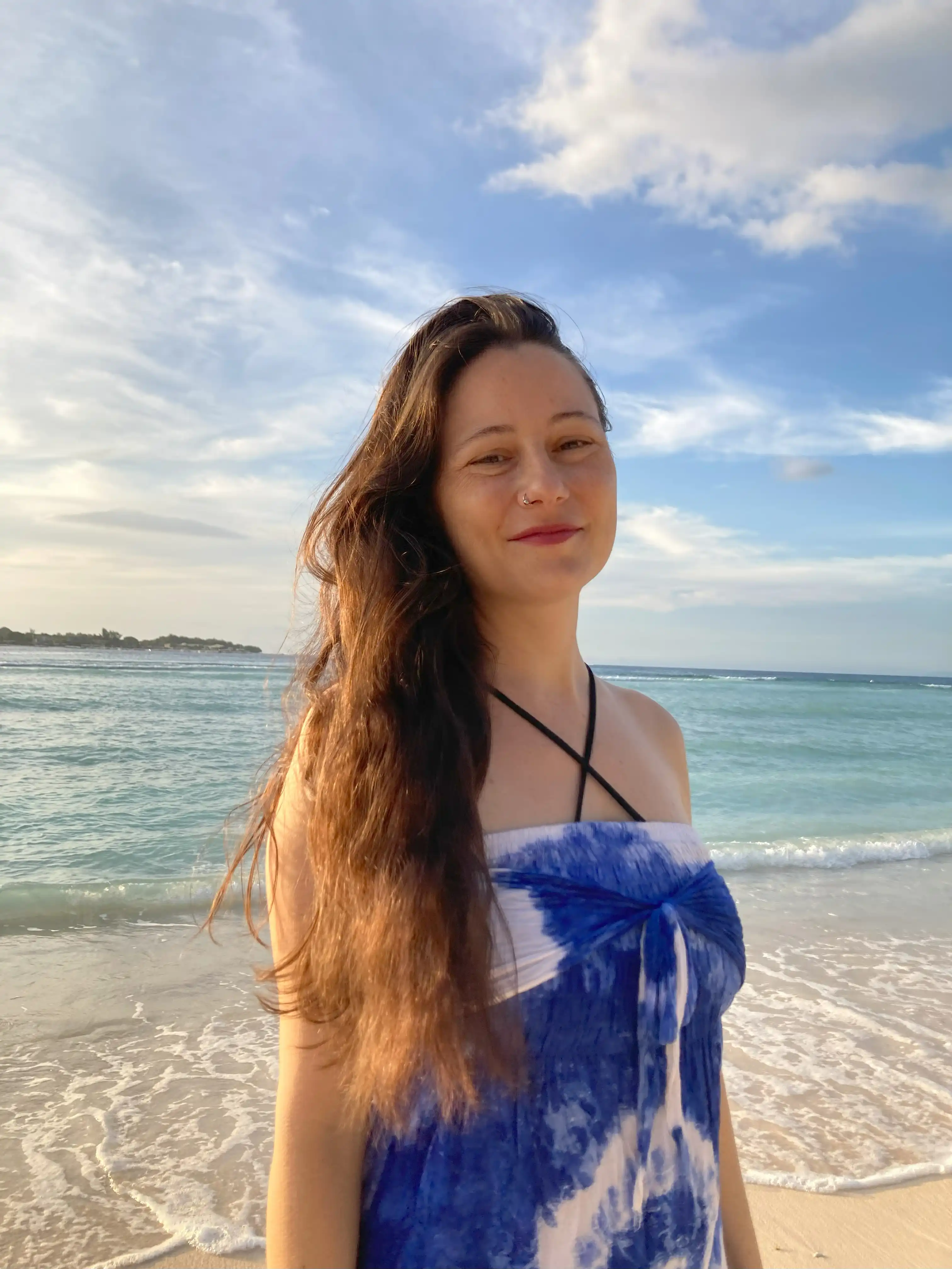 Carla by the Ocean – Personal Note for the Bali Retreat Carla standing by the ocean under a clear blue sky, sharing a personal note for the Bali retreat.