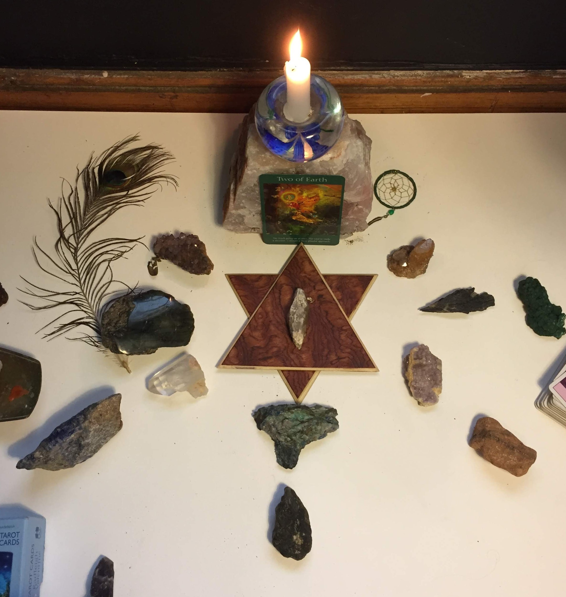 Sacred altar with candle, crystals, feather, and tarot card arranged for spiritual guidance and energy healing.