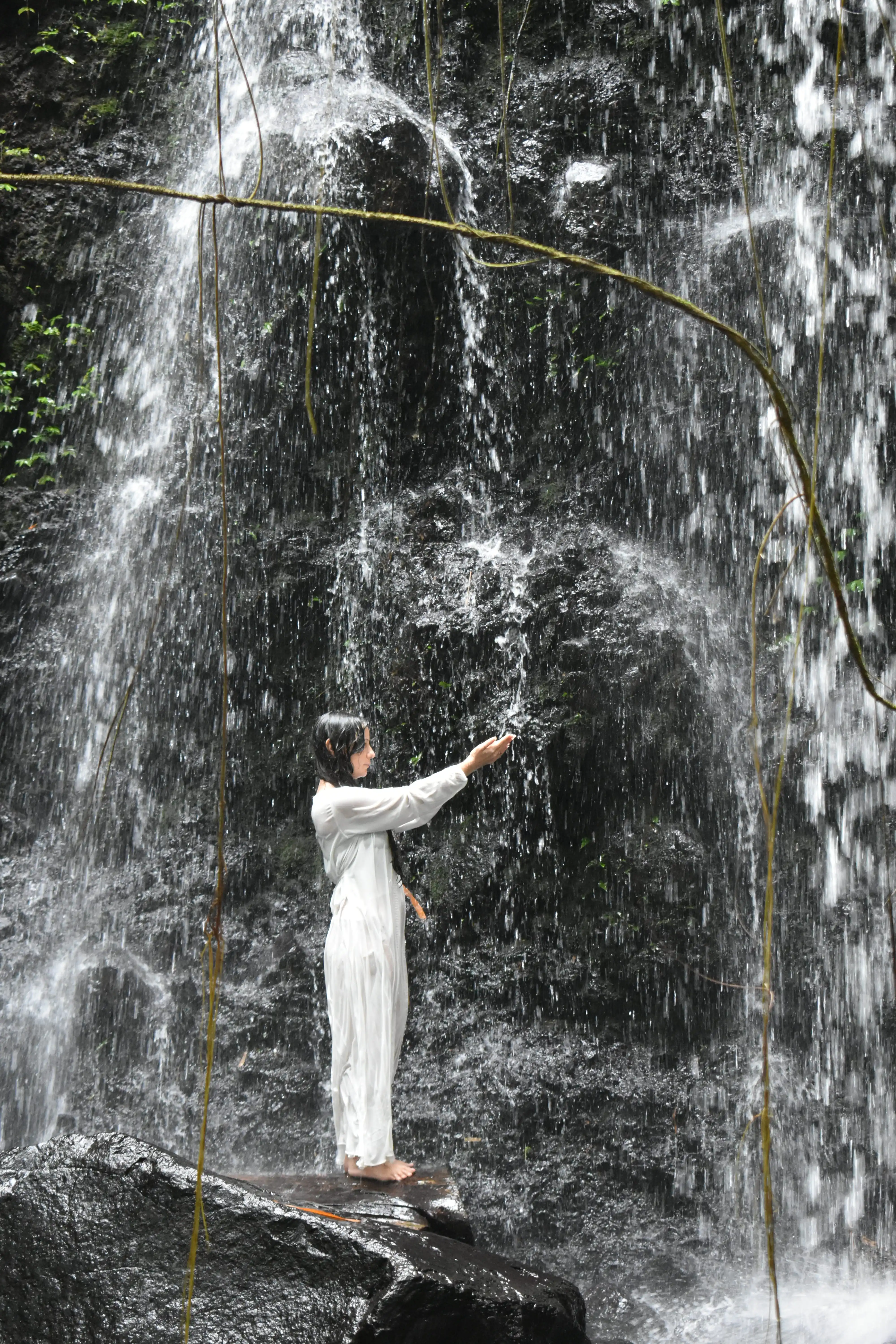 Psychic Carla standing directly under a powerful jungle waterfall in Tabanan, Bali, during a sacred water purification ritual.