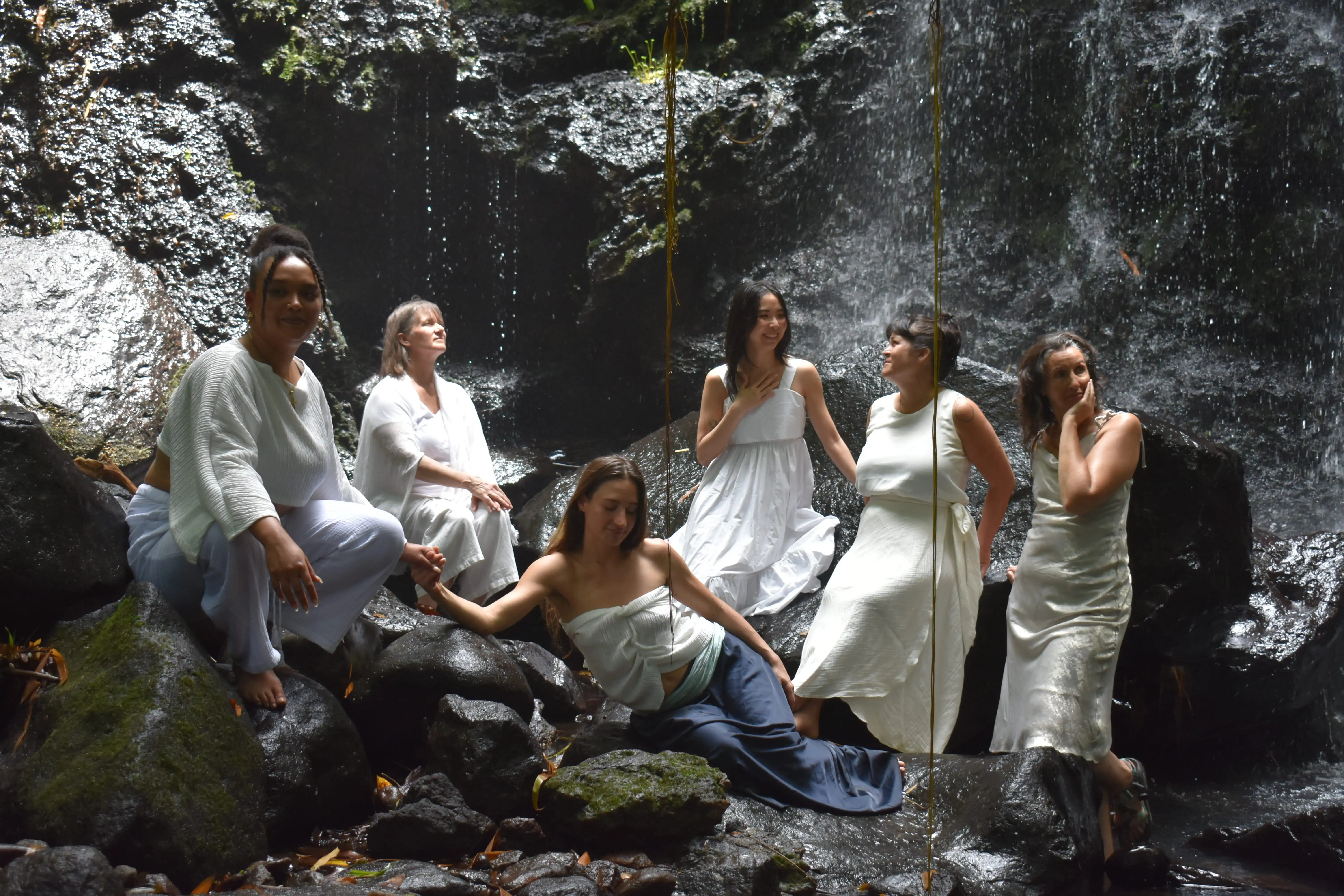 women in white ceremonial clothing sitting together at the base of a Tabanan waterfall