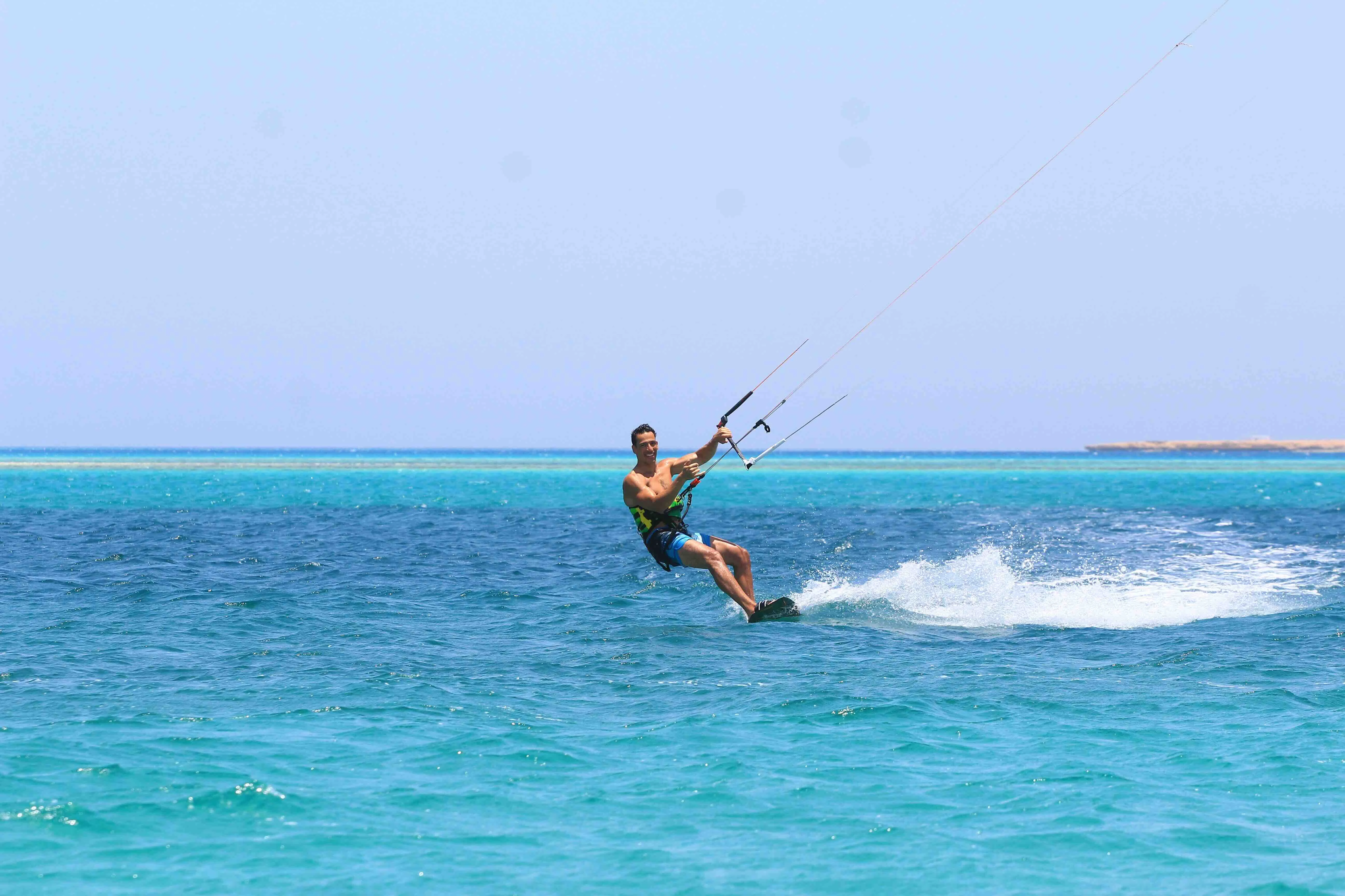 A person kiteboarding in the crystal-clear waters of the Red Sea, Egypt, under a clear sky.